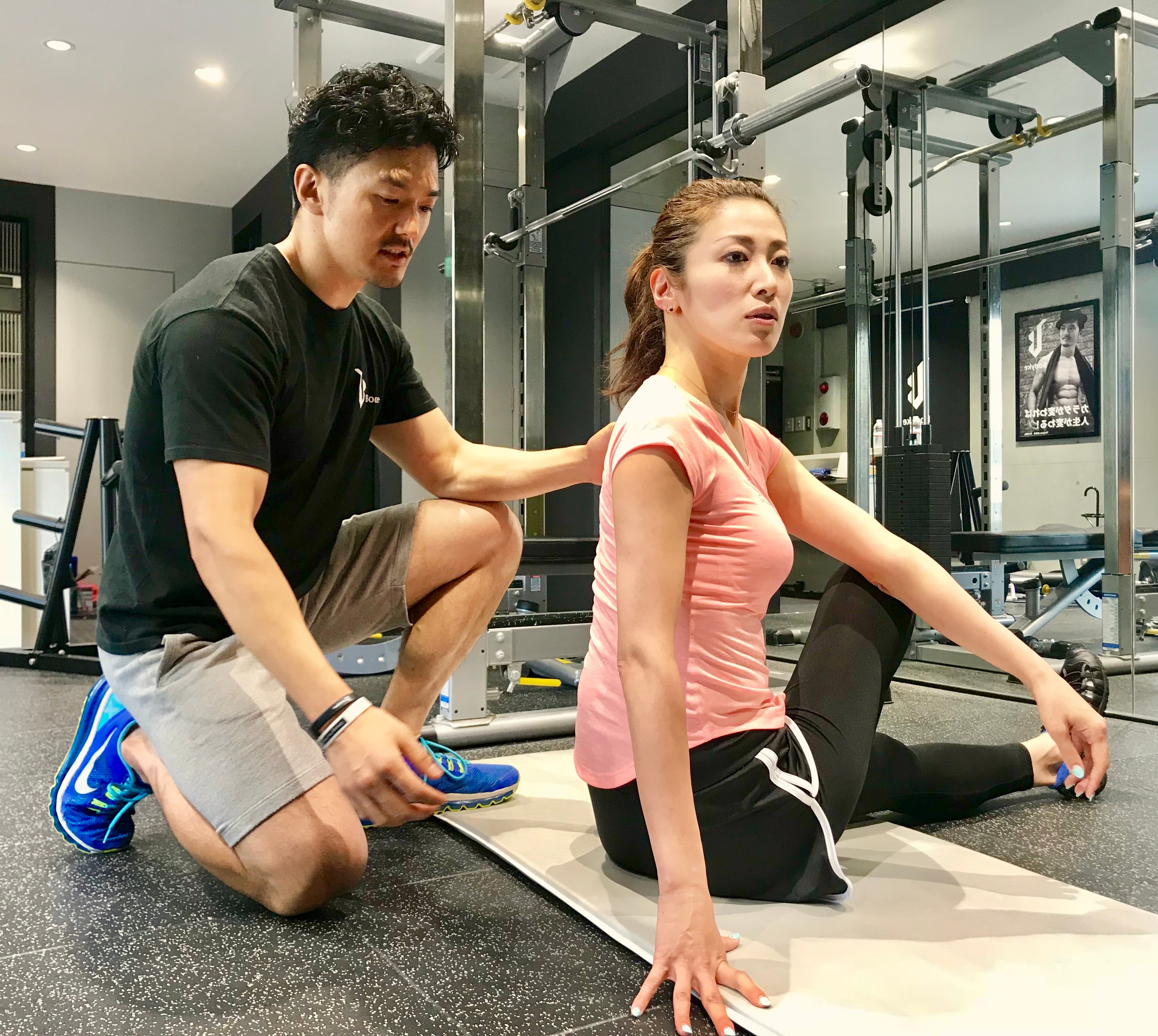 パーソナルジムでストレッチする女性とサポートするトレーナー