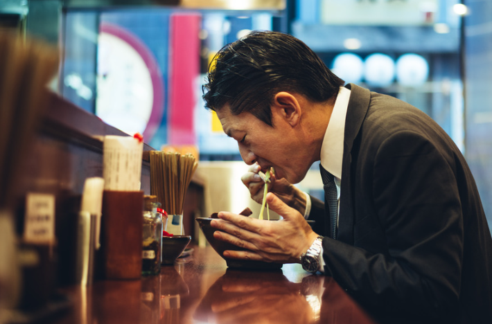 ラーメンをすするスーツを着た男性