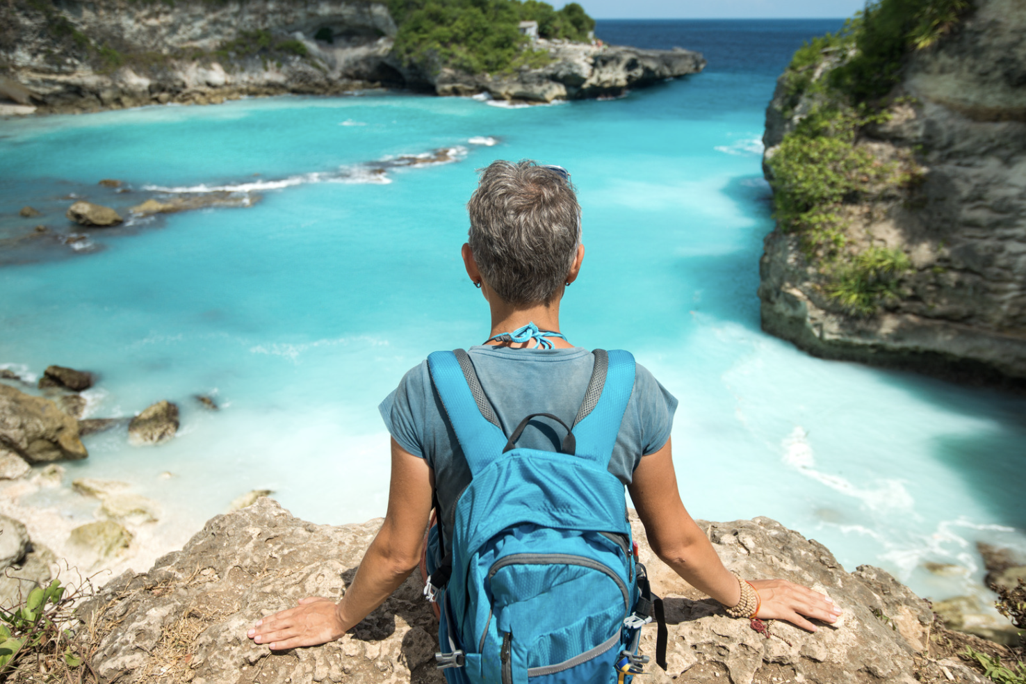 崖のふちに座って海を見下ろす男性